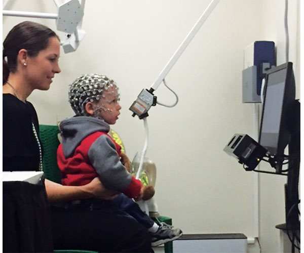 A child and parent in a testing center. The child is wearing a headset and looking at a computer monitor.